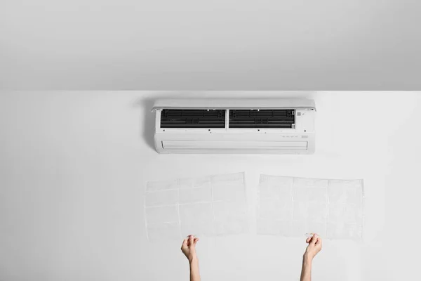 Woman holding filters under air conditioner indoors, closeup