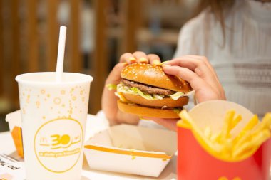 McDonald 's burgerli kadın, patates kızartması ve kafedeki masada içki, yakın plan.