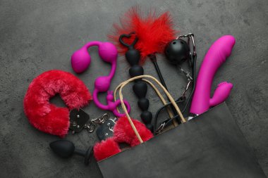 Gri masa üzerinde farklı seks oyuncakları olan kağıt alışveriş torbası.