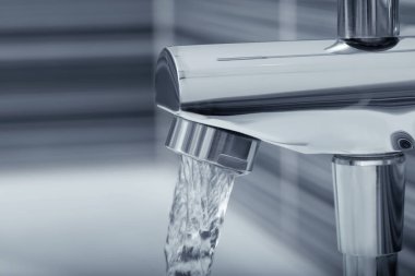 Water flowing from bath tap on blurred background, closeup