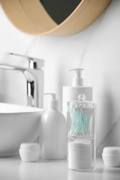 Containers with cotton swabs and pads near cosmetic products on white countertop in bathroom