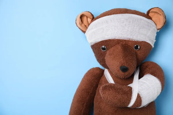 Toy bear with bandages on light blue background. Space for text