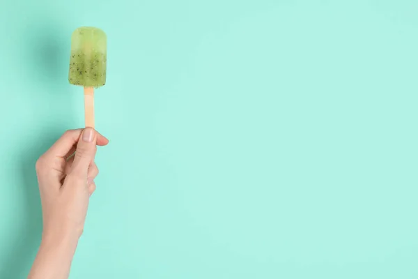 Woman holding delicious ice pop on turquoise background, closeup view with space for text. Fruit popsicle