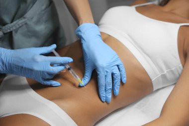 Genç bir kadın kuaförde göbek iğnesi yaptırıyor.