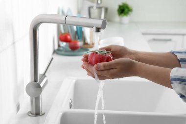 Woman washing fresh ripe tomato under tap water in kitchen, closeup