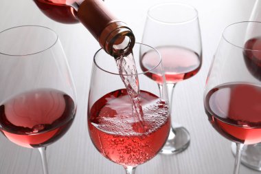 Pouring rose wine from bottle into glasses on wooden table, closeup clipart