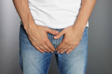 Gri arka planda genital uçuktan muzdarip bir adam, yakın plan.