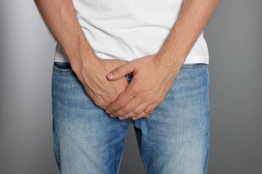 Gri arka planda genital uçuktan muzdarip bir adam, yakın plan.
