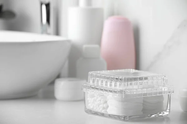 Container with cotton swabs and pads near cosmetic products on white countertop in bathroom. Space for text