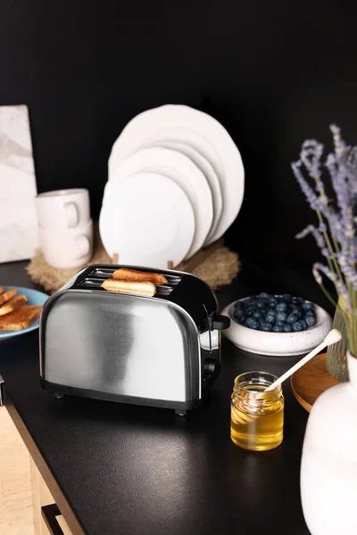 烤面包和蜂蜜放在厨房黑色台面上的烤面包机 — 图库照片