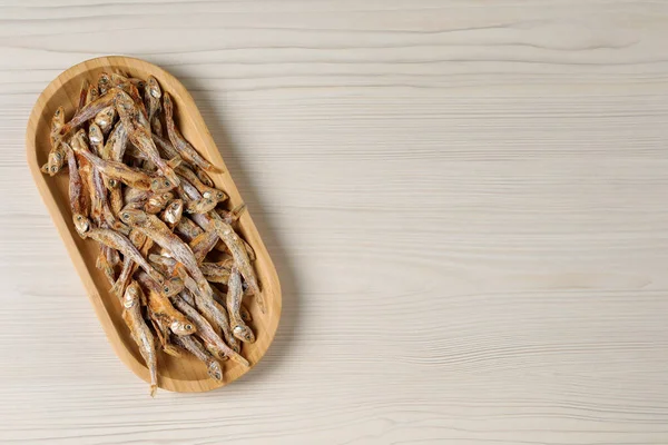 Plate of tasty dried anchovies on light wooden table, top view. Space for text