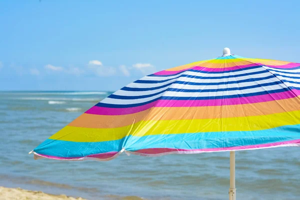 Colorful striped beach umbrella near sea sunny day, closeup