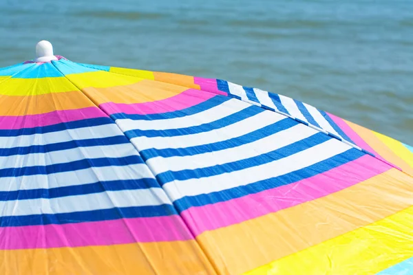 Colorful striped beach umbrella near sea, closeup