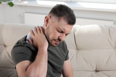 Evdeki kanepede ısıtma yastığı kullanan bir adam.