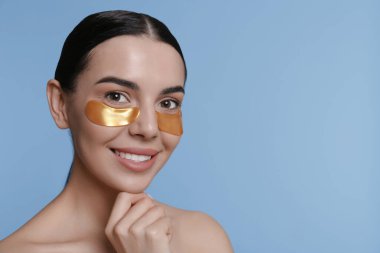 Açık mavi arkaplanda göz altı yamaları olan güzel genç bir kadın.