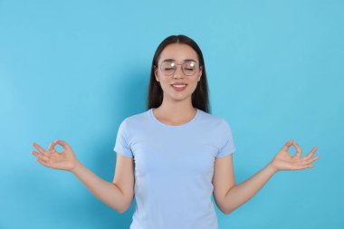 Zen bul. Güzel genç bayan açık mavi arka plan üzerinde meditasyon yapıyor.
