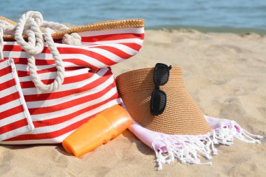 Stylish striped bag with beach accessories on sand near sea