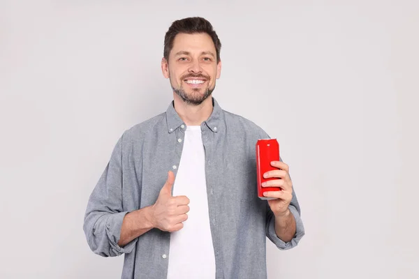 快乐的男人拿着红罐 拿着饮料 用浅灰的背景展示大拇指 — 图库照片