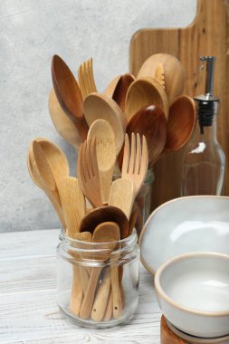 Farklı mutfak gereçleri ve bulaşık takımı beyaz ahşap masada, dokulu duvara karşı.