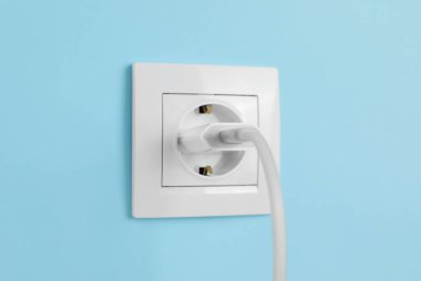 Şarj adaptörü açık mavi duvardaki güç prizine takıldı. Elektrik arzı