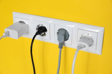 Power sockets with inserted plugs on yellow wall, closeup. Electrical supply