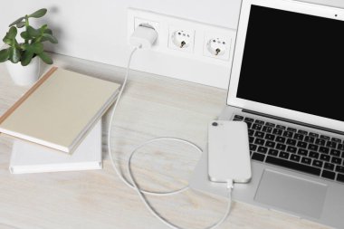 Laptop ve akıllı telefon ahşap masada şarj oluyor.