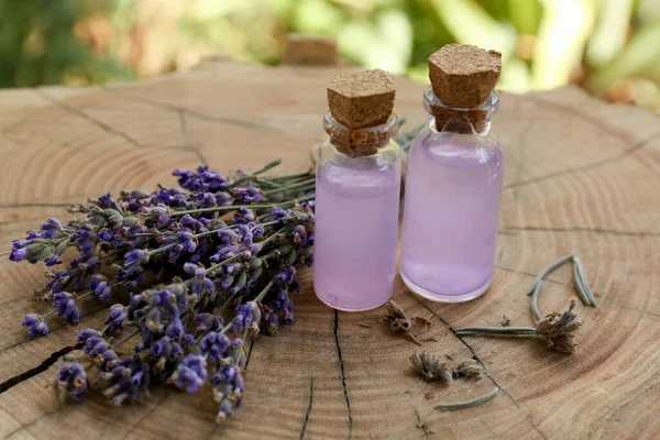 Beautiful lavender flowers and bottles of essential oil on wooden stump, closeup