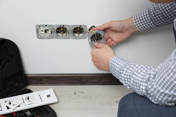 Электрик с отверткой для ремонта розетки в помещении, крупный план