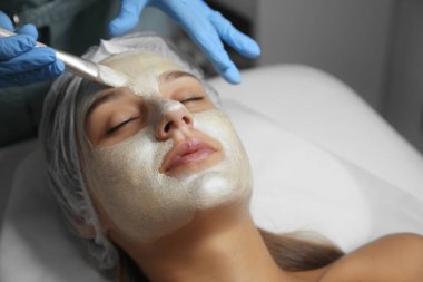 Spa salonu müşterinin yüzüne maske uygulayarak güzellik uzmanı