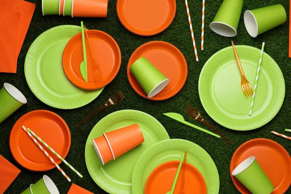 Disposable tableware on green artificial grass, flat lay