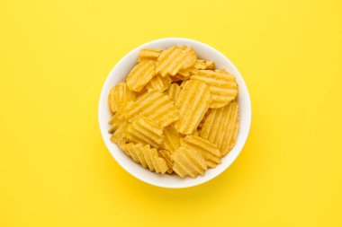 Sarı arka planda bir kase lezzetli patates cipsi.