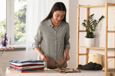 Young woman folding clothes at white table indoors
