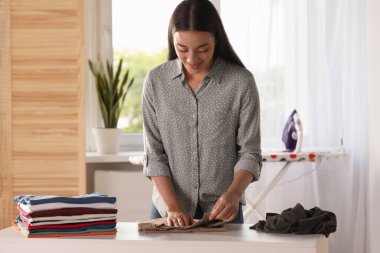 Young woman folding clothes at white table indoors