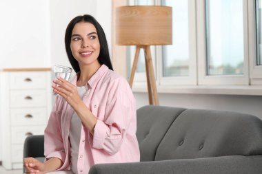 Kapalı alanda bir bardak suyu olan genç bir kadın. Tazeleyici içecek.