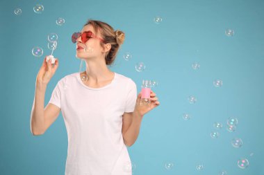 Açık mavi arka planda sabun köpüğü üfleyen genç kadın, metin için boşluk