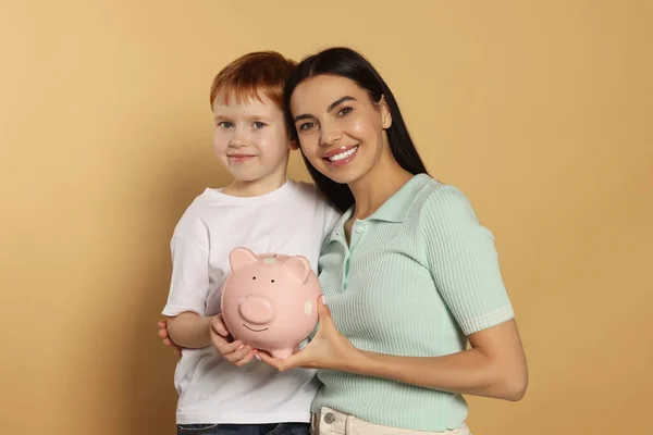 Mutter Und Ihr Sohn Mit Keramik Sparschwein Auf Beigem Hintergrund — Stockfoto