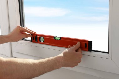 Worker using bubble level after plastic window installation indoors, closeup
