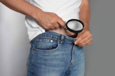 Gri arka planda büyüteçle yakın çekim yapan bir adam. Genital uçuk