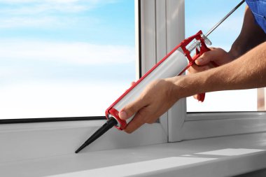 Worker sealing plastic window with caulk indoors, closeup. Installation process