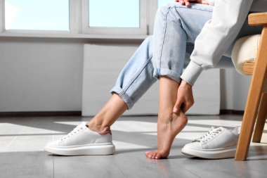 Woman rubbing sore foot at home, closeup