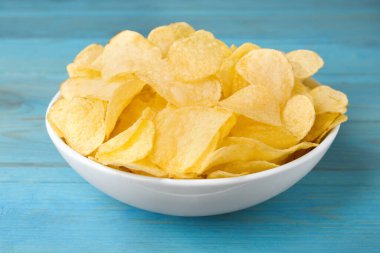 Açık mavi ahşap masada patates cipsli kase, yakın plan.