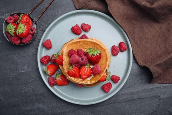 Tasty pancakes served with honey and berries on black table, flat lay