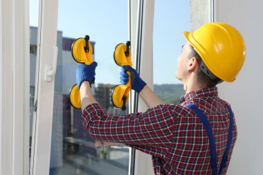 Worker using suction lifters during plastic window installation indoors