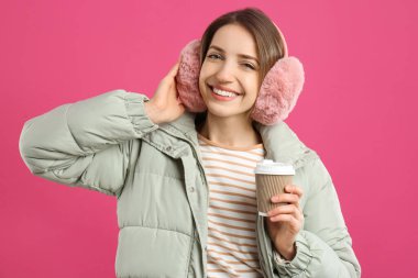 İçkili mutlu kadın pembe arka planda sıcak kulaklık takıyor.