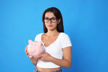 Açık mavi arka planda domuz kumbaralı gözlüklü genç bir kadın.