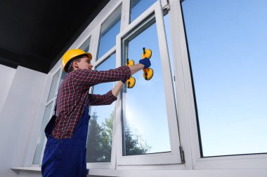 Worker using suction lifters during plastic window installation indoors