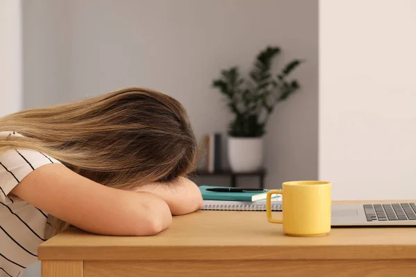 Woman sleeping in front of laptop at wooden table indoors