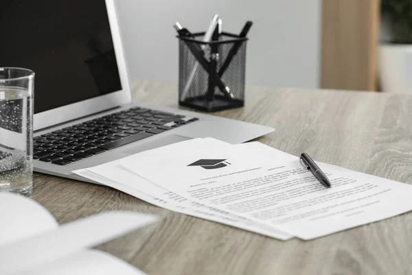 Acceptance letters from universities and laptop on wooden table indoors, closeup