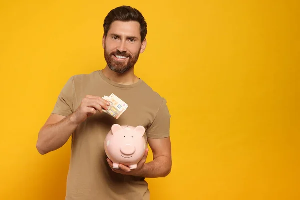 Happy Man Putting Money Piggy Bank Orange Background Space Text — Stock Photo, Image