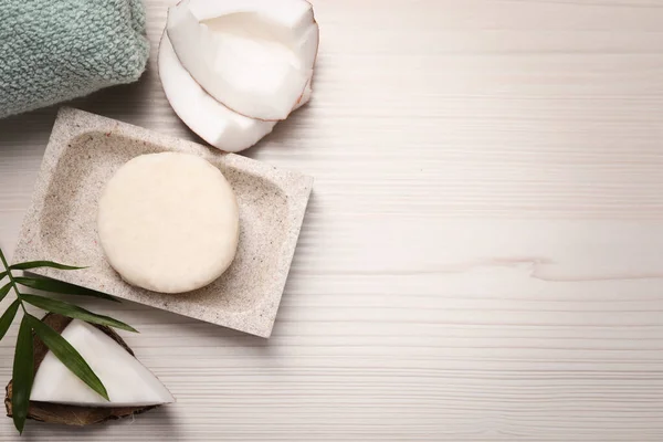 Solid shampoo bar, leaf and coconut on white wooden table, flat lay. Space for text